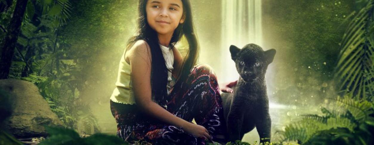 Dziewczynka siedząca w dżungli na tle wodospadu. U jej prawego boku siedzi mały czarny Jaguar Dziewczynka siedząca w dżungli na tle wodospadu. U jej prawego boku siedzi mały czarny Jaguar