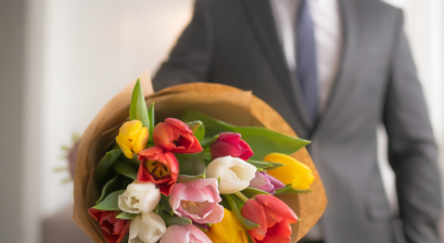 tło to rozmyty meżczyzna trzymający bukiet kwiatów który wyciągniety jest w stronę aparatu 