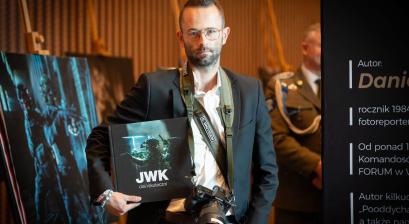 Daniel Dmitriew z albumem na tle swojej fotografii 