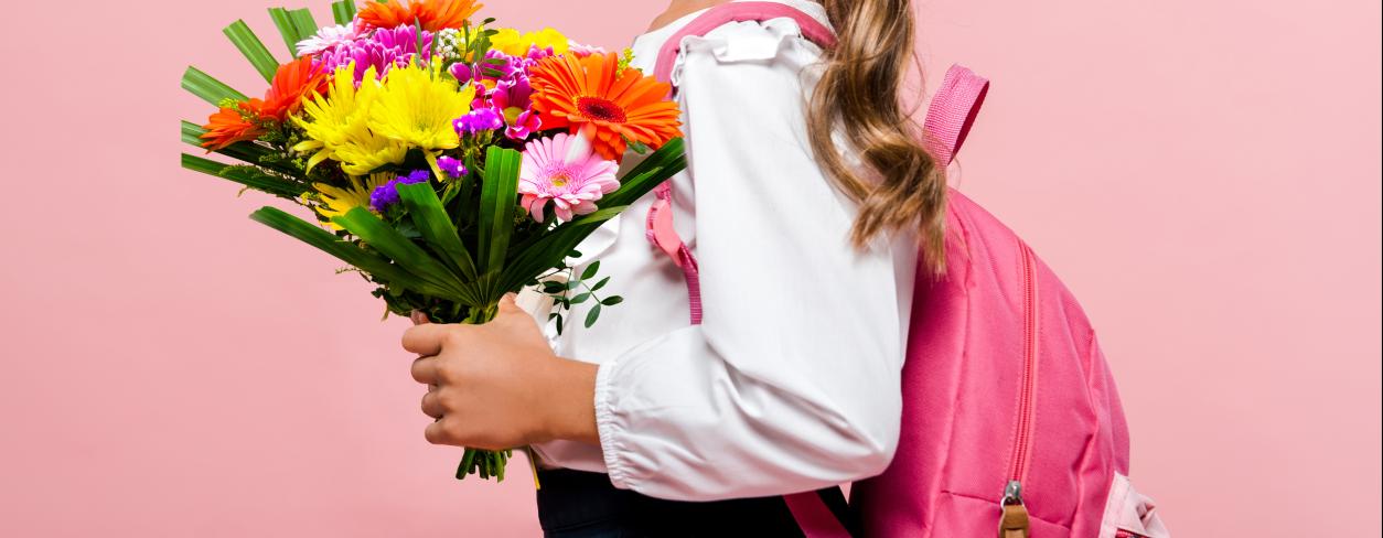 dziewczynka odświętnie ubrana z bukietem kwiatów z różowym plecakiem na plecach 