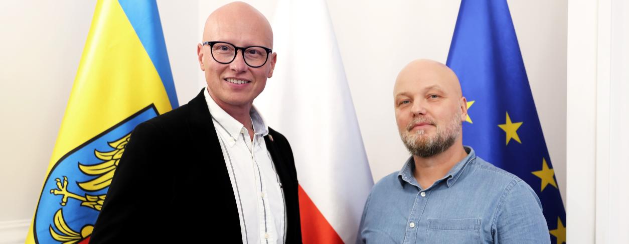 zdjęcie zastępcy burmistrza oraz pana Piotr Walendziuk na tle flagi Lublińca polski, oraz unii Europejskiej 