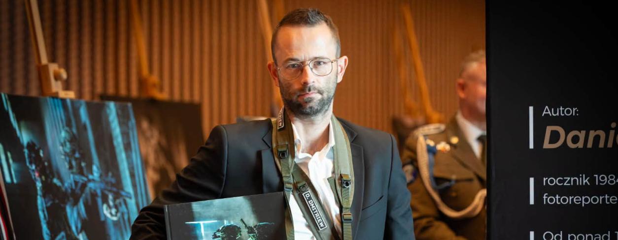 Daniel Dmitriew z albumem na tle swojej fotografii 