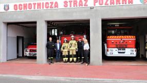 Strażacy ochotniczej straży pożarnej przed bramą, wjazdowa dla wozów strażackich, strażak i strażaczka wraz z Burmistrzem i Zastępcą miasta Lublińca